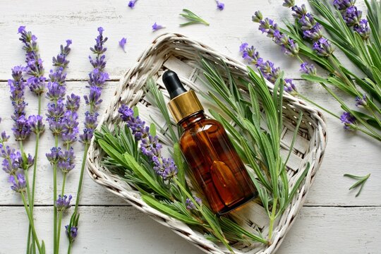 Lavender oil in a bottle with lavender flowers in a basket on white old wooden background top view