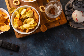 A popular set of sports fans - beer, chips, snacks. There is also a baseball glove with a ball and a remote control on the table. Watching a baseball game with friends, sports, friendship.