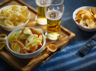 Light beer in glasses, chips, snacks, onion rings. TV remote. Blue background. High angle view. Watching movies, sports TV programs with friends. Advertising, banner, poster.