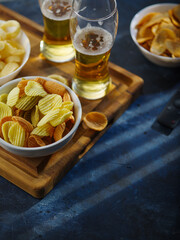 Beer, chips, other fast food on a wooden tray. TV remote. Concept - watching your favorite TV shows, sports programs on TV in the company of friends. High angle view.