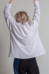 Caucasian blond woman posing with her hands up and back to camera in a white shirt.