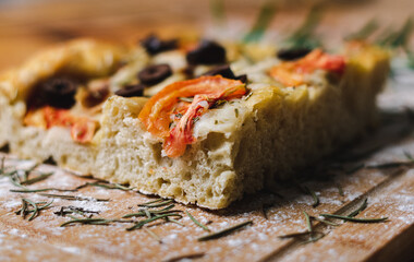 focaccia artesanal con tomates, aceitunas, cebollas en tabla y mesa de madera con harina alrededor
