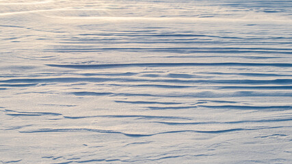 Snowy background, snow-covered surface of the earth after a blizzard in the morning in the sunlight with distinct layers of snow