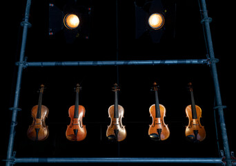 Five violins or violas hanging within a steal bar frame with two stage lights creating some ambient...