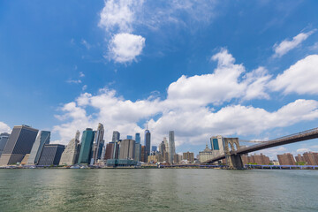 Fototapeta premium Unique shape summer clouds float over the Lower Manhattan skyscraper and Brooklyn Bridge along the East River on June 20, 2021 in the Brooklyn Borough of New York City NY USA.