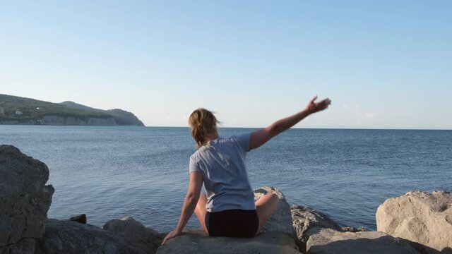 Caucasian woman doing stretching exercises at seashore. Girl meditating at the view of the ocean or sea at sunrise. Concept of yoga and solo activity. Meditation and healthy lifestyle