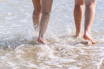 two women running into water on beach in the sea, closeup of legs