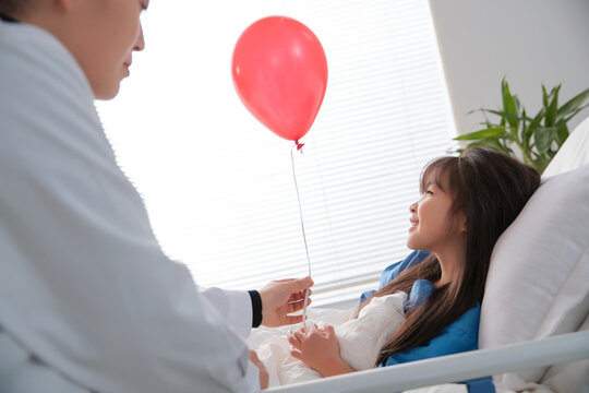 Young woman doctor to examine bed girl with a red balloon

