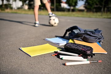 Scattered school supplies and workbooks falling out of an open backpack, lie on the asphalt of the...