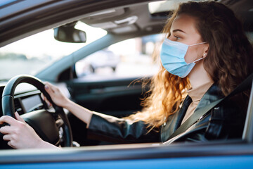 Fototapeta na wymiar Young woman in protective medical mask driving a car. Covid-2019. Transport isolation.