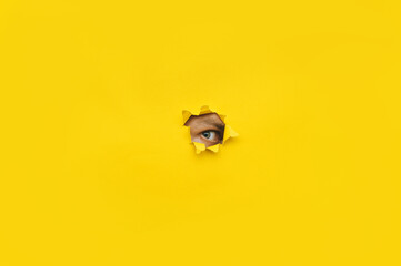 Eye looking through a hole in a yellow paper. Voyeurism. The man is watching the wife. A curious look. Jealousy, spying on or overhearing the concept. Copy space.