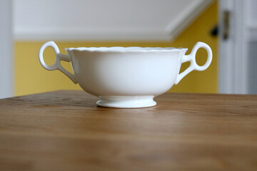 White china sugar bowl with two handles standing on wooden table