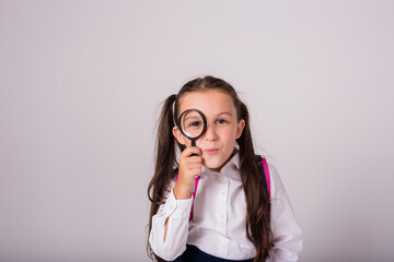 cheerful brunette schoolgirl in uniform and holding a magnifying glass on a white background with a place for text