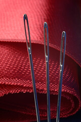 three sewing needles on a red fabric background. close-up.