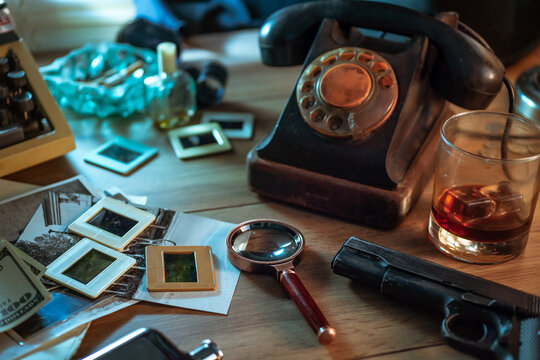 Private detective's desk, noir still life with a vintage phone, typewriter, lamp, gun and retro photos