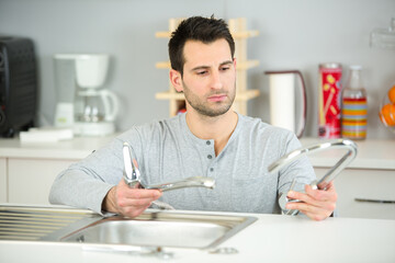 happy attractive young man fixing tap in the kitchen