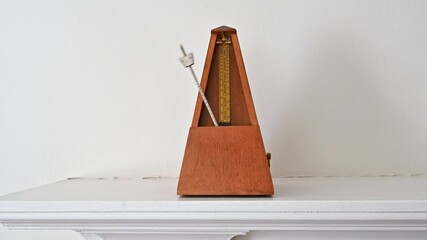 An old fashioned metronome beating at a Largo pace on a white shelf.