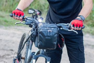 A cyclist in gloves near a mountain bike with a bag on the handlebars.