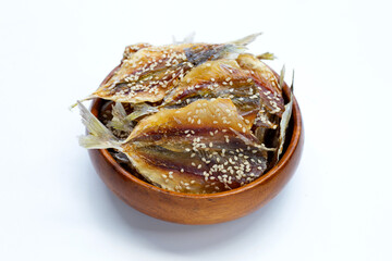 Dried fish with sesame seeds in wooden bowl on white background.