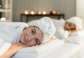 Two young woman friends lying down and relaxing on massage beds preparation for facial treatment and beauty therapy in spa salon.