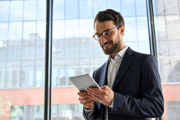 Smiling mature Caucasian bearded businessman executive manager in glasses holding tablet device...