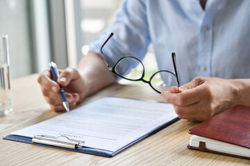 Businesswoman lawyer reading trust partnership contract sit at table in office holding glasses in...