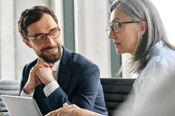 Happy smiling bearded businessman in eyewear with clasped hands listening to female executive manager ceo mentor in glasses. Professional business people discuss business plan at board room meeting.