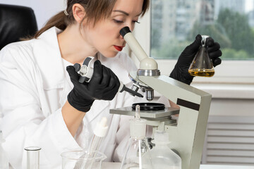 Laboratory assistant with microscope in his hands. Woman researcher. She is looking at something...