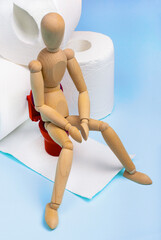 Wooden dummy sits on a roll of toilet paper. Digestion, bowel problems concept. Diarrhea or...