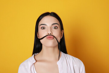 Funny woman making fake mustache with her hair on yellow background