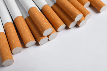 Pile of cigarettes with orange filters on white background, closeup. Space for text