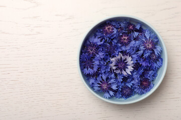 Beautiful colorful cornflowers in bowl on white wooden table, top view. Space for text