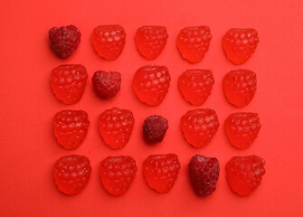 Delicious gummy candies and fresh raspberries on red background, flat lay