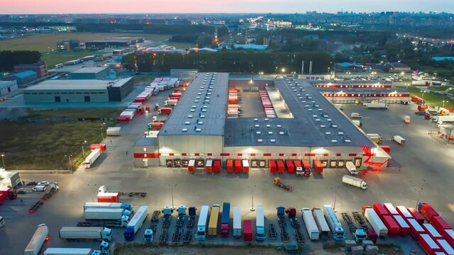Aerial hyper lapse (hyperlapse - motion time lapse) of a logistics park with a loading hub. Semi-trailer trucks standing at warehouse ramps for loading and unloading goods in the evening