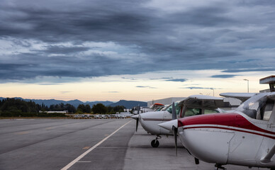 Fototapeta na wymiar Airplanes parked at the Airport Apron during a dramatic cloudy sunset. Pitt Meadows, Greater Vancouver, British Columbia, Canada.