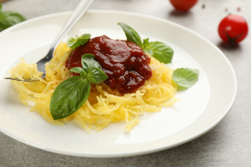 Tasty spaghetti squash with tomato sauce and basil served on light grey table, closeup