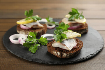 Delicious sandwiches with salted herring, onion rings, parsley and lemon on wooden table, closeup