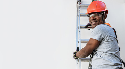 Confident young Latin male carpenter in hardhat holding drill and looking at camera with smile...