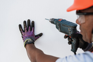 Confident Latin male holding drill on wall.