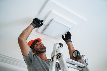 Latino electrician installing a led light on the ceiling. - Powered by Adobe