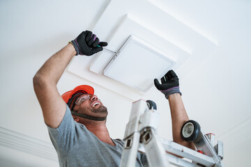 Latino electrician installing a led light on the ceiling.