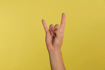Teenage boy showing rock gesture on yellow background, closeup