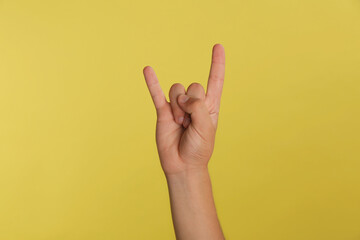 Naklejka premium Teenage boy showing rock gesture on yellow background, closeup