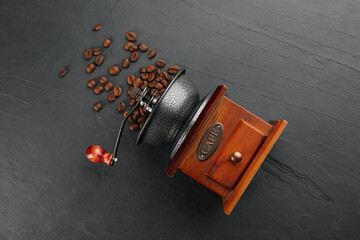 Vintage manual coffee grinder with beans on black table, flat lay