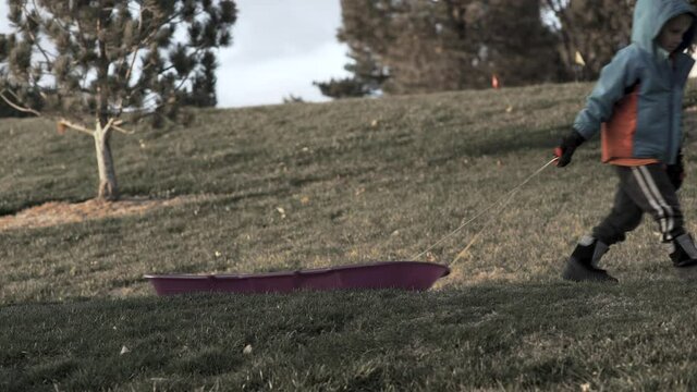 Boy pulls a sled in a snowless winter hoping for snow to come.