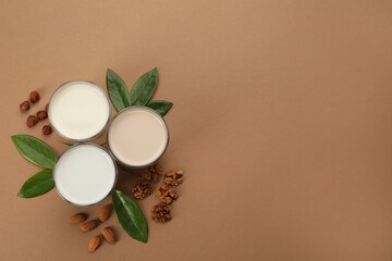 Obraz na płótnie Canvas Different vegan milks and nuts on brown background, flat lay. Space for text