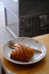 Fresh french croissant on white ceramic plate on wooden table