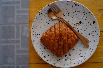 Fresh french croissant on white ceramic plate on wooden table