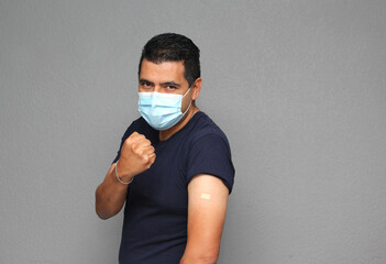 Healthy Latino adult man with mask showing his arm that recently received the Covid-19 vaccine
