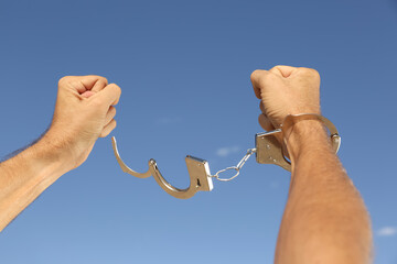 Man in handcuffs against blue sky outdoors, closeup